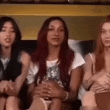 three women are sitting next to each other on a couch and talking to each other .