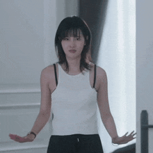 a woman in a white tank top and black pants is standing with her arms outstretched