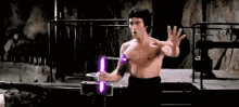 bruce lee is holding a purple light saber in a dark room .
