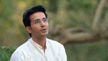 a man wearing glasses and a white shirt is sitting in a park .