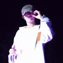 a man wearing a hat and a white shirt with the letter k on it is holding a microphone