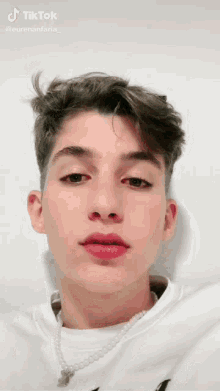 a young man wearing a pearl necklace is looking at the camera .