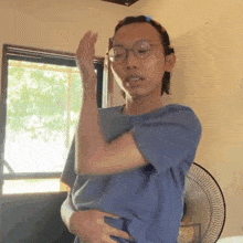 a young man wearing glasses and a blue shirt is standing in front of a fan