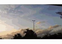 a sunset with a street light in the foreground and trees in the background