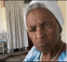 an older woman wearing a white headband and a pearl necklace makes a face