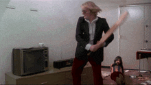 a man in a suit is holding a bat in front of a tv