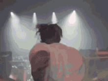 a man in a white shirt is standing on a stage in front of a crowd in a dark room .