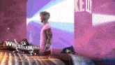 a man in a pink shirt stands in front of a wrestlemania sign
