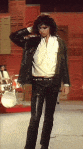 a man in a leather jacket and white shirt is standing on a stage