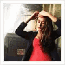 a woman in a red dress is standing in front of a wall and adjusting her hair .