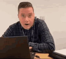 a man in a plaid shirt is sitting at a desk with a laptop .