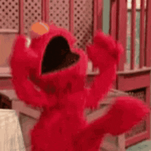 elmo from sesame street is dancing in a room with his arms outstretched .