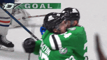 a hockey player in a green jersey celebrates a goal with his teammate