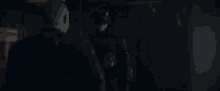 a man in a batman costume is standing in a dark room holding a gun .