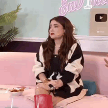 a woman is sitting on a pink couch with her legs crossed and a microphone in her hand .