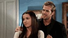 a man and a woman are standing next to each other and the man is looking at the woman 's hair