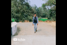 a young man is walking down a road with a youtube logo on the bottom right