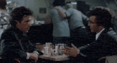 two men are sitting at a table with a soda can that says sol