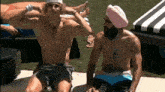 a shirtless man wearing a pink hat sits next to another man