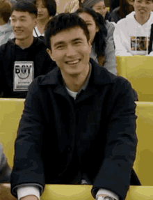 a man is smiling while sitting in a crowd of people in a classroom .