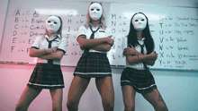 three girls wearing masks standing in front of a white board with the alphabet written on it