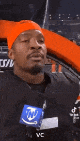 a man wearing an orange headband and a black shirt is talking on a microphone .