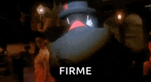 a man in a hat and a red shirt is standing in a dark room with the word firme written in front of him .