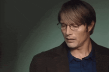 a man wearing glasses and a blue shirt is looking at the camera .