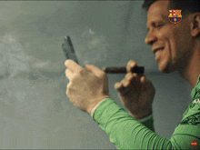 a man in a green shirt smoking a cigar with the fcb logo on his shirt