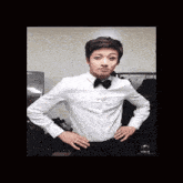 a young man wearing a white shirt and a black bow tie is standing with his hands on his hips .
