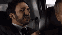 a man in a suit and tie is talking to another man in the back seat of a car