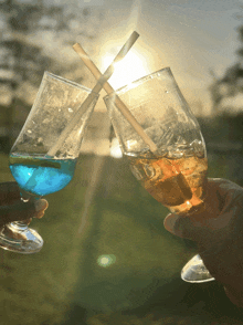 two glasses with straws in them are being held up in front of a sunset