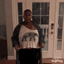a woman wearing a crop top with an elephant on it is standing in front of a door .