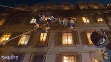 a group of smurfs hanging from a rope in front of a building