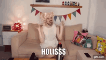 a man in a white dress is sitting on a couch with the word holisss on the bottom