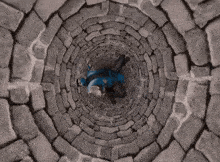a person in a blue jacket is laying down in a stone well