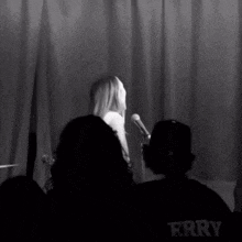 a man in a black shirt with the word ferry on it sits in front of a microphone
