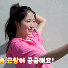 a woman in a pink shirt is smiling in front of a wall with korean writing on it