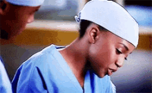 a female surgeon wearing scrubs and a white headband is looking down .