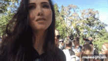a woman with long dark hair is standing in front of a crowd of people in a park .