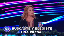 a woman holds a glass of water in front of a sign that says buscaste y eligeste una presa