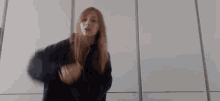 a woman in a black sweatshirt is dancing in front of a white wall