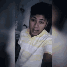a young man in a yellow and white striped shirt is making a funny face .