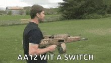 a man is holding a gun in a field with the words `` aa12 wit a switch '' .