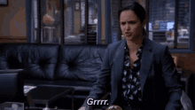 a woman in a suit is sitting on a leather couch and making a face .