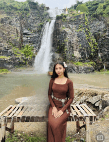 a woman in a brown dress is sitting in front of a waterfall with the letter c on the bottom