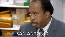 a man in a suit and tie is making a funny face and says san antonio .