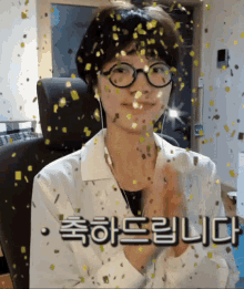 a woman wearing glasses and ear buds is surrounded by gold confetti and says " 축하 드립니다 "