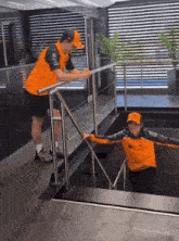 a man in a mclaren shirt helps another man climb a set of stairs