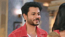 a man with a beard wearing a red jacket is looking at a woman in a room .